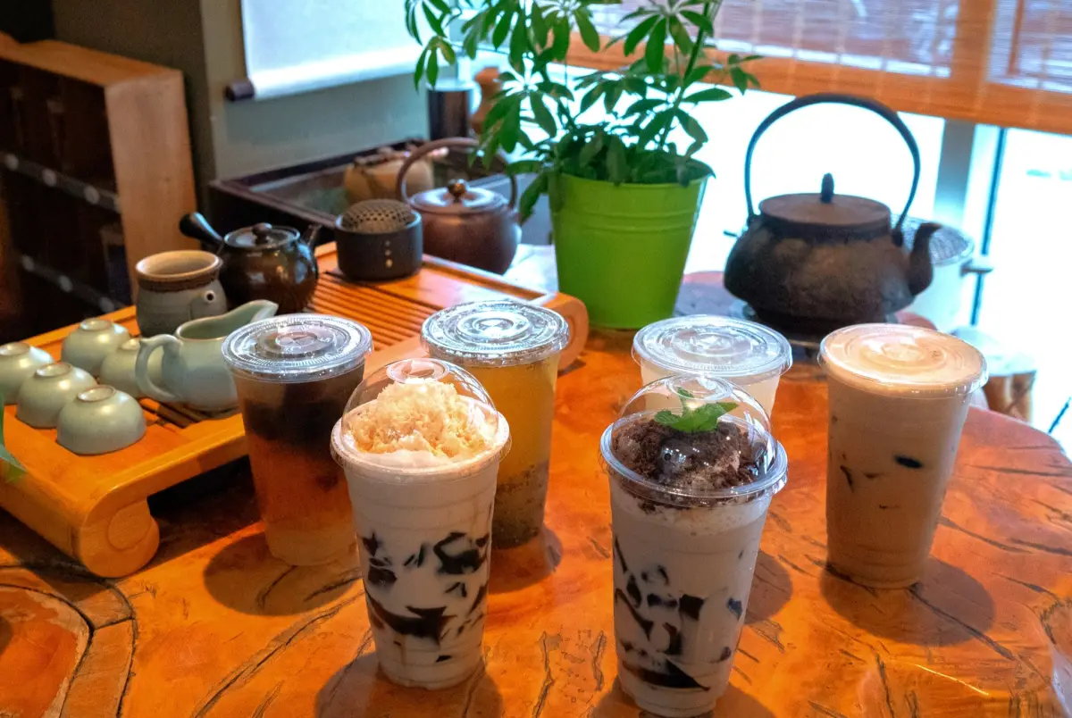 Grass jelly drinks and teas on a wooden tea table at Health Station, with teapots and a potted plant